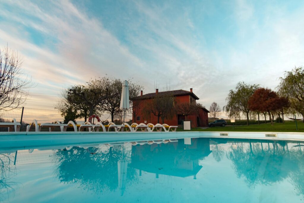 A tranquil backyard pool reflects a charming house and serene sky. Perfect for relaxation.